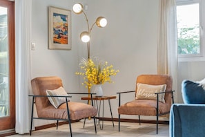 A room with two brown armchairs, a small table with a vase of yellow flowers, a wall-mounted painting, and a floor lamp with three lights. - Private Pool · BBQ · Gorgeous Pool (Noord)
