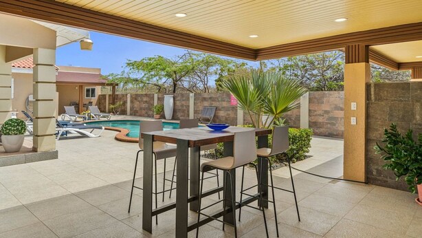 Um pátio externo com piscina, espreguiçadeiras e uma mesa com cadeiras.
