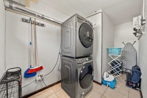 A laundry room with stacked washers and dryers, a mop, a laundry basket, and a portable ironing board. - Private Pool · BBQ · Gorgeous Pool (Noord)