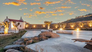 A serene outdoor area with a stone wall, a small building with a red roof, and a seating area with benches and a table. - Citadel Natural Stone Villa (Mykonos)
