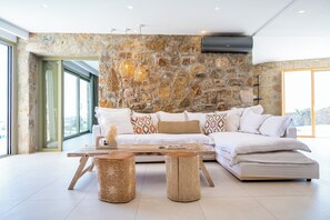 Ein modernes Wohnzimmer mit einer Steinwand, einem Ecksofa, einem Couchtisch und einem großen Fenster.