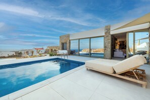 Ein moderner Poolbereich mit freiem Blick auf das Meer, einer Liege und einer Steinmauer.