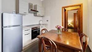Una cocina moderna con refrigerador, horno y estufa integrados, una mesa de madera con sillas y un florero con flores.