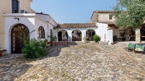 Un patio con suelo de adoquinado, edificios blancos con arcos y plantas en macetas.
