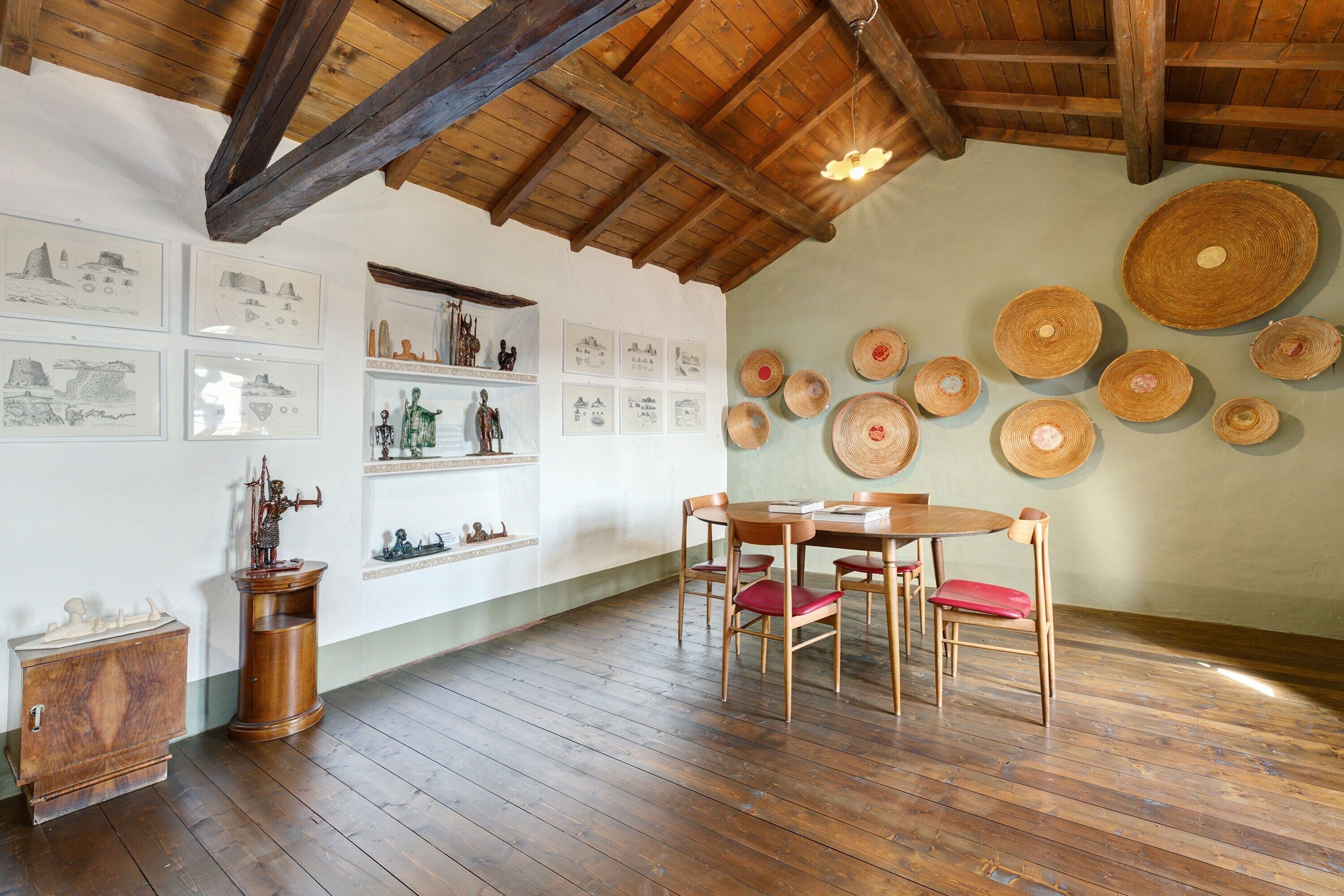 Ein Zimmer mit Holzbalken, einem Holztisch mit Stühlen und Körben an der Wand.