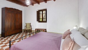 Un dormitorio con una cama, un armario de madera, una silla, una mesita y una ventana.