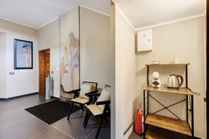 A hotel lobby with a tiled floor, a coffee machine, a kettle, a fire extinguisher, and a wooden shelf.