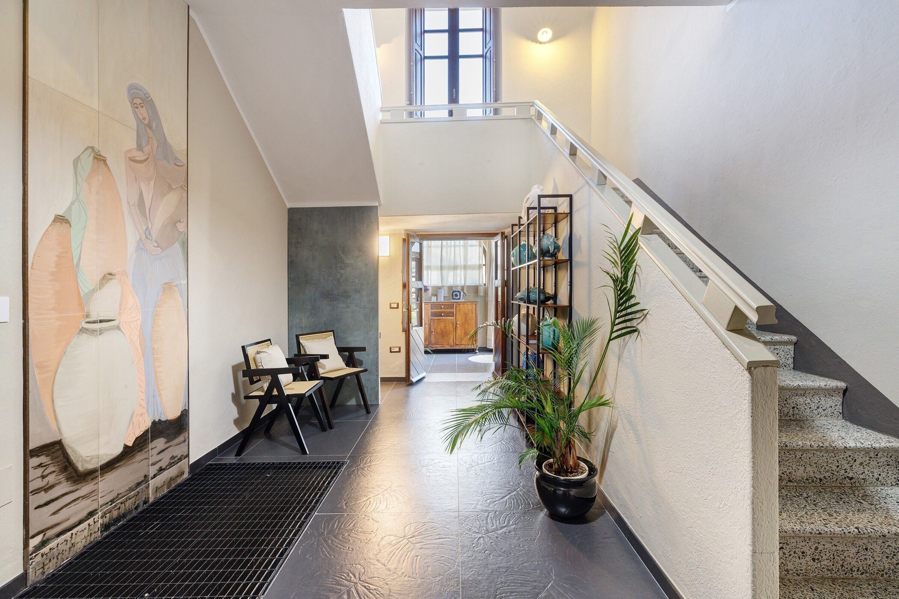 A hallway with a staircase, a mural, a seating area, and a potted plant.