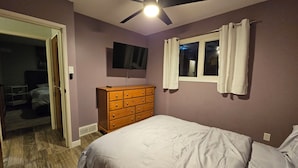 A bedroom with a bed, a dresser, a ceiling fan, a TV, and a window with curtains.