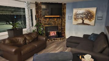 A living room with a stone fireplace, leather sofas, a flat-screen TV, and a painting on the wall.