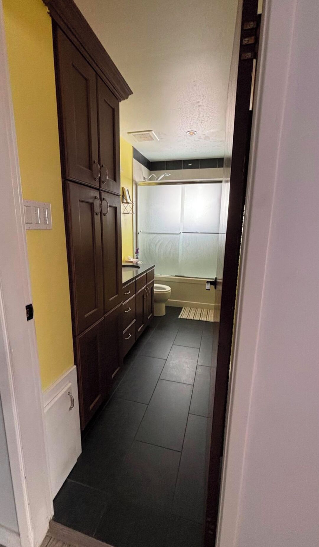 Een smalle gang die leidt naar een badkamer met toilet, wastafel en douche.