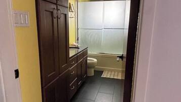Een smalle gang die leidt naar een badkamer met toilet, wastafel en douche.