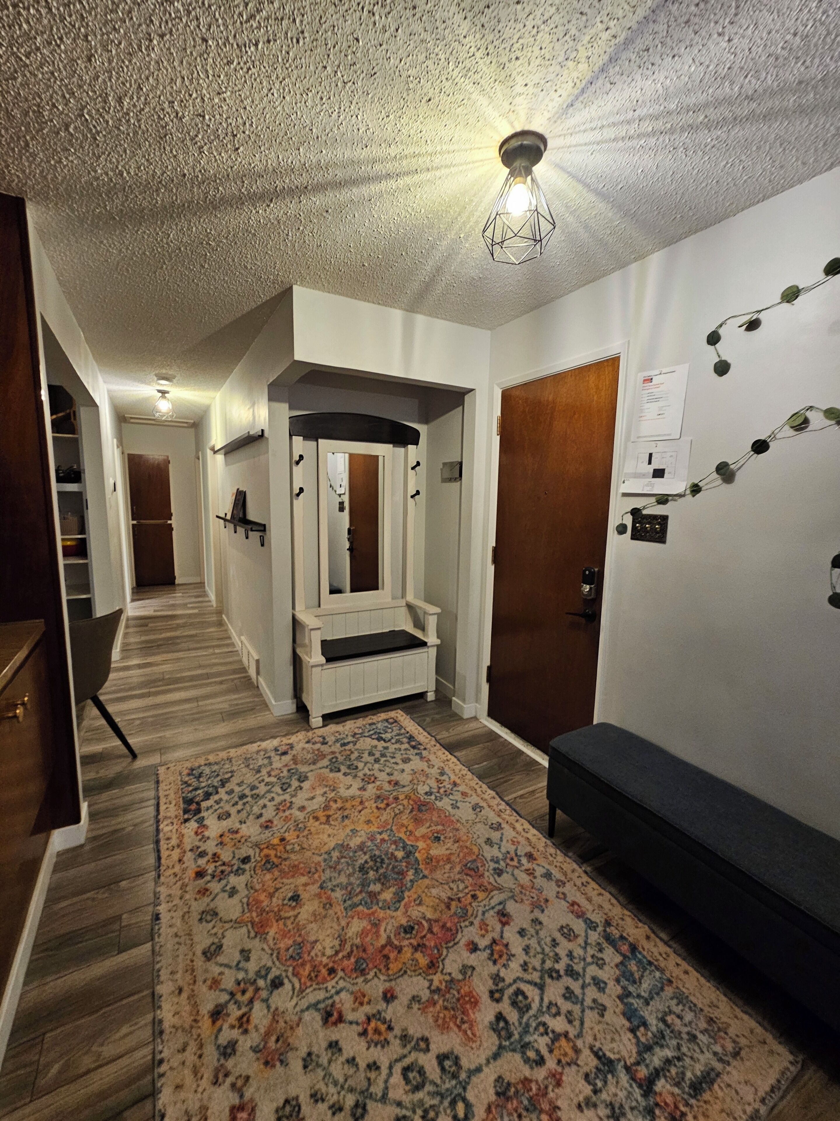 A hallway with a bench, a rug, and a mirror.