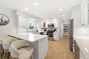 Une cuisine moderne avec des meubles blancs, un îlot central et un four encastré.