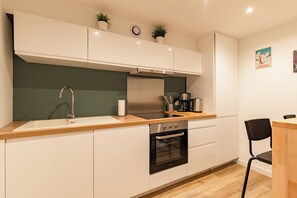 Eine moderne Küche mit weißen Schränken, einer Edelstahl-Dunstabzugshaube, einem eingebauten Backofen, einer Holz Arbeitsplatte und einem schwarzen Stuhl.