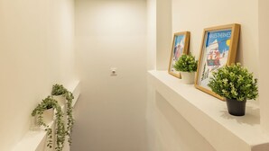 Uma escada estreita com paredes brancas, um corrimão e duas plantas em vasos no patamar.