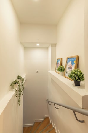 Eine schmale Treppe mit weißen Wänden, einem Geländer und zwei Blumentöpfen auf der Landung.