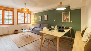 Sala de estar moderna com sofá, mesa de jantar e vista através de grandes janelas.
