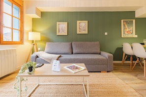 Ein Wohnzimmer mit einer Couch, einem Couchtisch mit einer Zeitschrift, einer Lampe und gerahmten Bildern an der Wand.