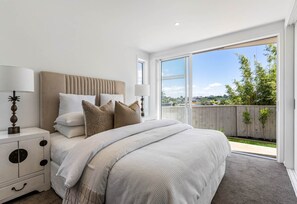 A bedroom with a large bed, bedside tables, a nightstand, and a sliding glass door leading to a balcony. - Charming 3-bedroom House With Ocean Views in Auckland (Auckland)