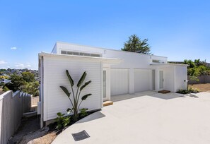 A modern, single-story building with a flat roof, large windows, and a small attached garage. - Charming 3-bedroom House With Ocean Views in Auckland (Auckland)