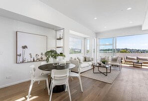 A modern living room with a dining area, large windows, and a view of the city. - Charming 3-bedroom House With Ocean Views in Auckland (Auckland)