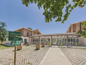 A building with a covered entrance, wooden barrels, and directional signs for 'Bâtiment A' and 'Bar'. - The Swallow - Apt for 4 - Shared Pool (Biscarrosse)