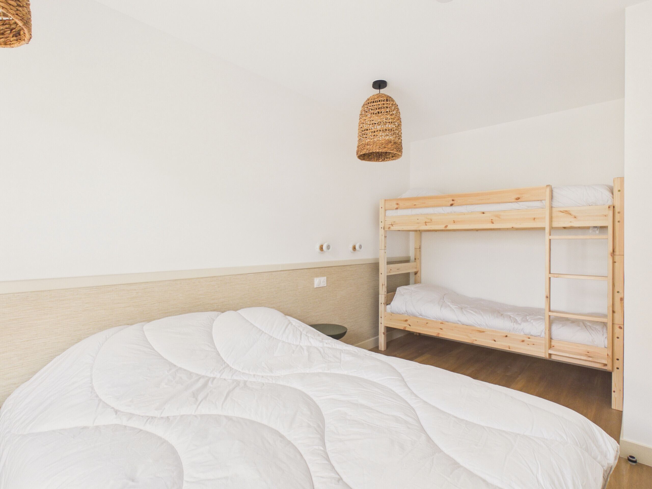 Ein Etagenbett mit weißer Matratze, einer gewebten Leuchte und einem Holzkopfstück.