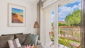 Un salon avec un canapé, des coussins, un tableau encadré et une vue sur l’extérieur grâce à une porte-fenêtre coulissante.