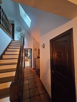 A staircase leading to a second floor with a skylight above, a wooden door, and a kitchen area in the background. - Lazo House · 5 bedrooms. Oceanfront · Beach within walking distance. Garden. 10 min from Paimpol (Plouézec)