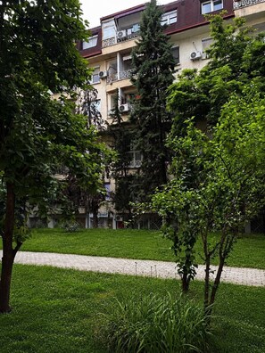 A multi-story residential building with balconies, surrounded by greenery and a paved walkway. - Cozy studio free public parking, near to City Center, Main train and bus station (Skopje)