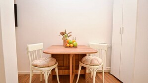 A dining area with a wooden table, two chairs, a fruit bowl, and a radiator. - Cozy studio free public parking, near to City Center, Main train and bus station (Skopje)