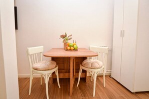 A dining area with a wooden table, two chairs, a fruit bowl, and a radiator. - Cozy studio free public parking, near to City Center, Main train and bus station (Skopje)