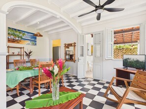 Ein Essbereich mit Schachbrettboden, Holzkstühlen, einem Tisch mit grüner Tischdecke und einer Vase mit Blumen.