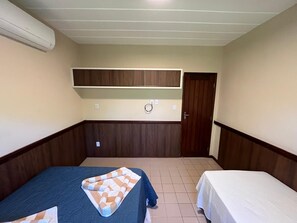 Una stanza piccola con due letti, un armadio in legno, una ventola a soffitto e un condizionatore d'aria.