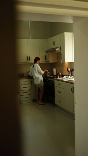 Una persona cucina in una cucina con mobili bianchi, un fornello e un piano di lavoro con diversi oggetti da cucina.