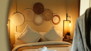 A bed with white linens, a bedside table with a lamp, and a wall with woven wall art.