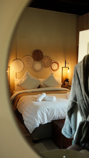A bed with white linens, a bedside table with a lamp, and a wall with woven wall art.