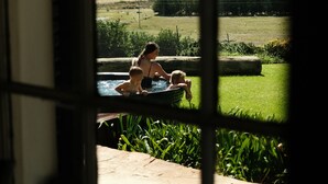 A view through a window with a metal grid, revealing a landscape with a swimming pool, a person, and a child.