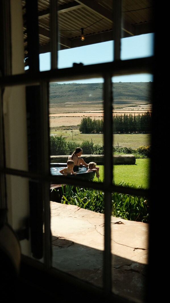 A view through a window with a metal grid, revealing a landscape with a swimming pool, a person, and a child.