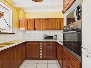 A kitchen with wooden cabinets, a microwave, a coffee maker, and a stove. - Apartment 100m from sea, terrace & BBQ (Les Anses-d´Arlet)