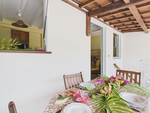 A dining table set with plates, glasses, and flowers, with chairs around it. - Apartment 100m from sea, terrace & BBQ (Les Anses-d´Arlet)
