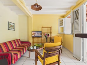 A living room with a sofa, a table with a vase, a television, and a chair. - Apartment 100m from sea, terrace & BBQ (Les Anses-d´Arlet)