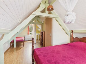 Ein Schlafzimmer mit schrägen Wänden, einem Bett mit rosa Decke, einem Holzschrank und einer Pendelleuchte.