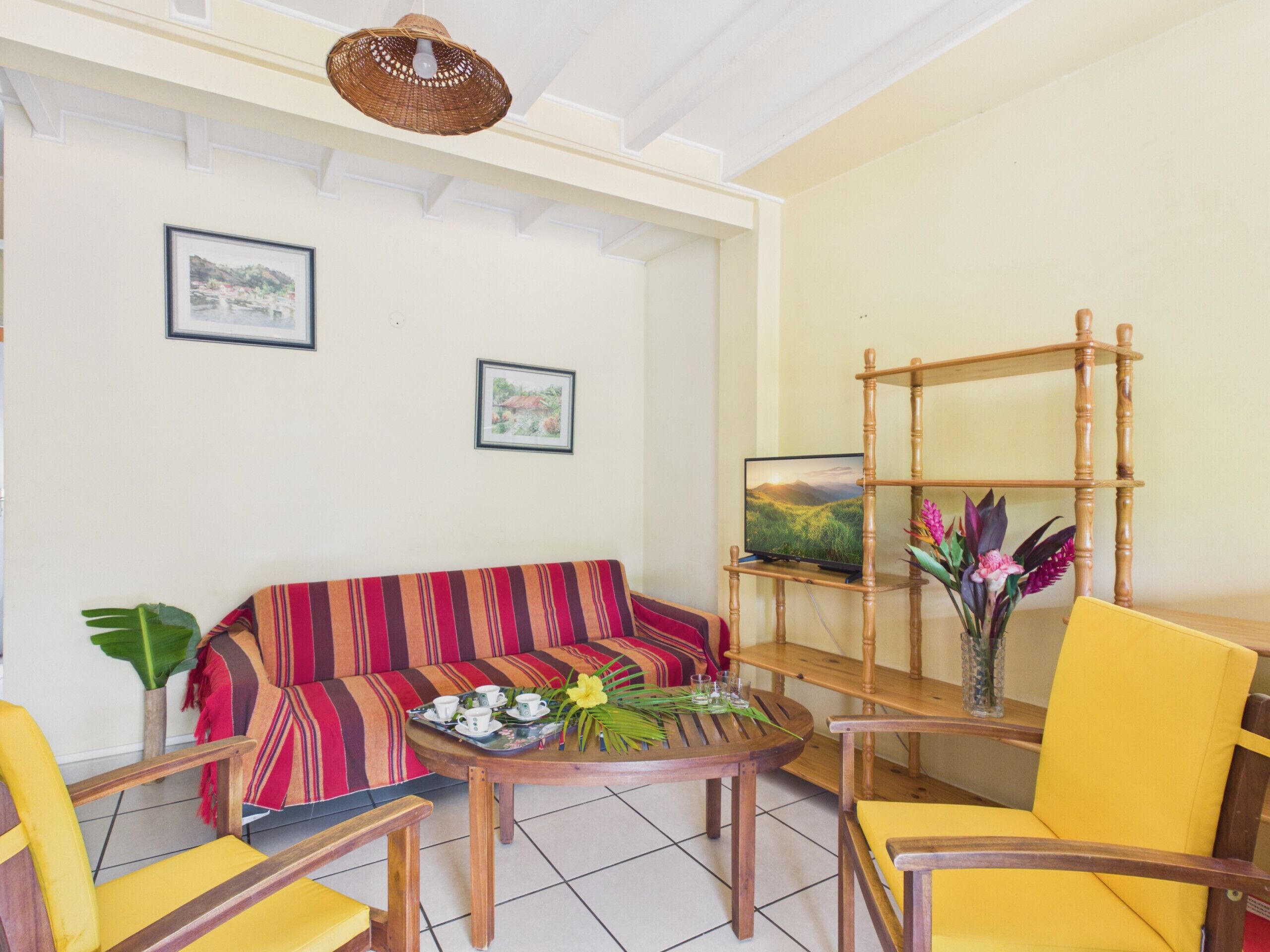 A room with a sofa, chairs, a table with a tray, a television on a wooden stand, and framed pictures on the wall.