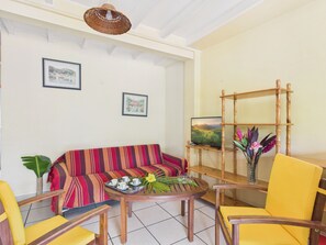 Ein Zimmer mit einer Couch, Sesseln, einem Tisch mit Tablett, einem Fernseher auf einem Holzboden und gerahmten Bildern an der Wand.