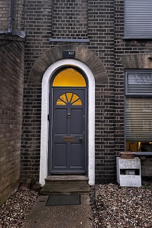 A dark grey door with a yellow arch above it, a brick wall, and a small white mailbox to the right.