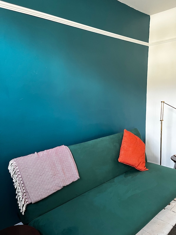 A teal-colored sofa with a patterned throw blanket and a single red pillow.