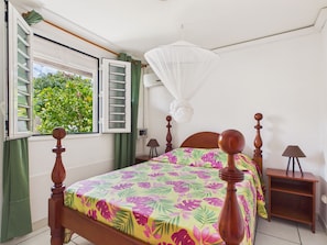Ein Schlafzimmer mit Bett, einem Fenster mit Blick auf Grünflächen, einem Nachttisch mit Lampe und einer Wand-Klimaanlage.
