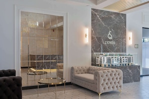 Een moderne lobby met een marmeren wand, een bank, een ronde tafel en een kroonluchter.